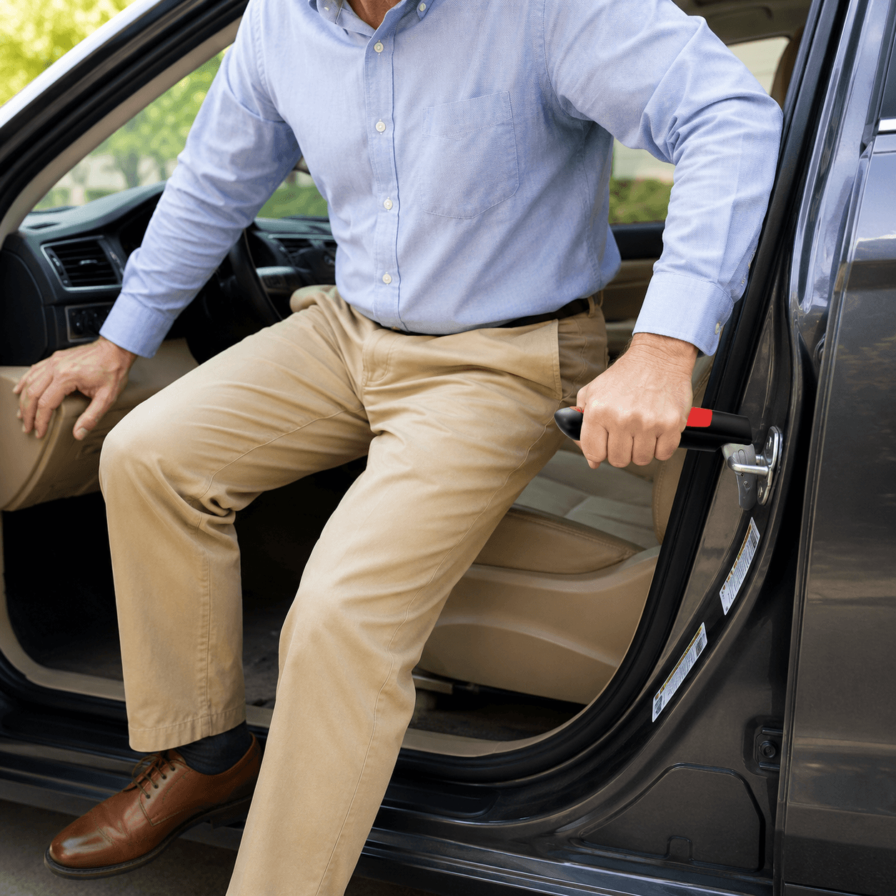 A man in a light blue dress shirt and khaki pants is stepping into a car through an open door, holding a handle with a red grip.